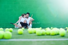 two people sitting on the ground with tennis balls in front of them and a dog