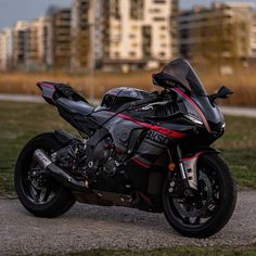 a black motorcycle parked on top of a dirt road next to grass and tall buildings