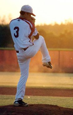 a baseball player pitching a ball on top of a pitchers mound at sunset with the sun behind him