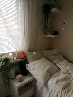 an unmade bed with white sheets and pillows in front of a window covered by sheer curtains