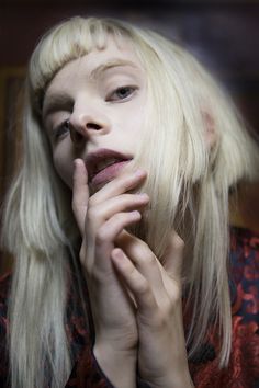 a woman with long blonde hair is posing for the camera while holding her hand to her face