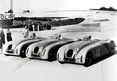 four race cars lined up on the tarmac with people standing around them looking at them