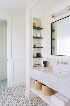 a bathroom with white walls and marble counter tops, along with open shelving on the wall