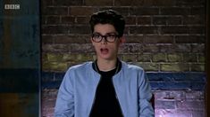 a young man wearing glasses standing in front of a brick wall with his mouth open