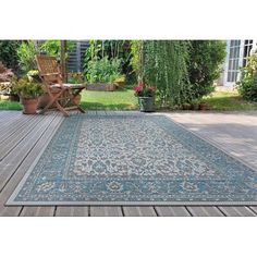 an outdoor area rug with wooden decking and chairs in the background, surrounded by greenery