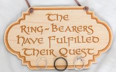 a wooden sign with two pairs of rings hanging from it's sides and the words ring - bearers have fulfilled their quest