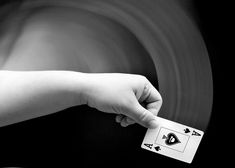 a hand holding a playing card in front of a black and white background