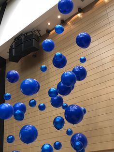 blue balloons are floating in the air near a white tiled wall and ceiling with lights