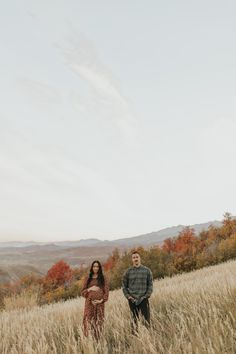 a man and woman standing in the middle of a field with tall grass on each side