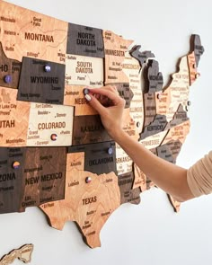 a person writing on a wooden map of the united states with magnets attached to it