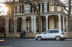 a white car parked in front of a yellow house next to a tree and fence