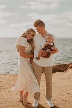 a man and woman holding a baby on the beach