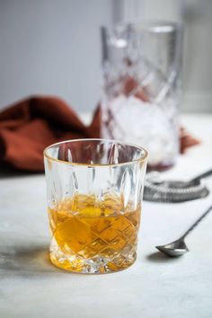 two glasses filled with liquid sitting on top of a table next to spoons and utensils