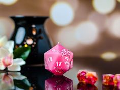 a pink dice sitting on top of a table next to other dices and flowers