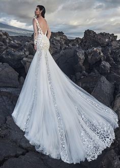 a woman in a wedding dress standing on rocks with her back turned to the camera