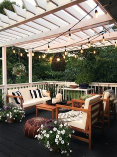 an outdoor patio with white furniture and string lights hanging from the pergolated roof