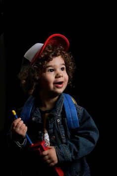 a little boy wearing a red hat and holding a baseball bat in his hand while standing against a black background