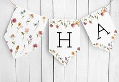 a banner with flowers hanging from it's sides on a white wooden wall next to the letters ah