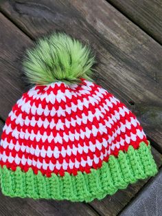 a red and white knitted hat with a green pom - pom