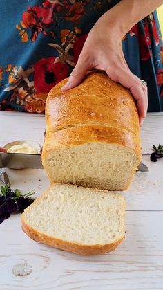 a person holding a loaf of bread on top of a white table next to flowers