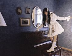 a woman standing next to a piano in a room with blue walls and pictures on the wall