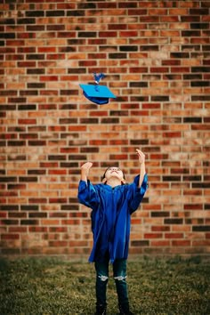 a young boy wearing a blue graduation gown is flying a kite in front of a brick wall