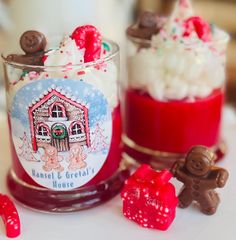 two glasses filled with desserts on top of a white table next to red and green candies