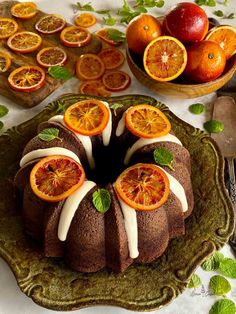 a bundt cake with oranges and mint leaves on the top, surrounded by other fruit