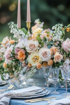 an arrangement of flowers in vases on a blue table cloth with silverware and candles