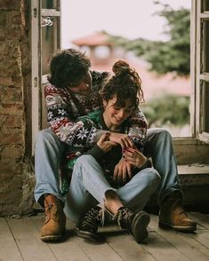 two people sitting on the floor in front of an open door looking at their cell phones