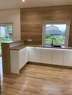 an empty kitchen with wooden floors and white cabinetry is shown in front of a large window