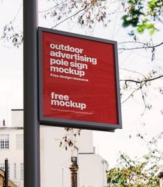 an outdoor advertising sign on a pole with trees in the foreground and buildings in the background