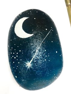 a painted rock with the moon and stars on it, sitting next to a pair of scissors