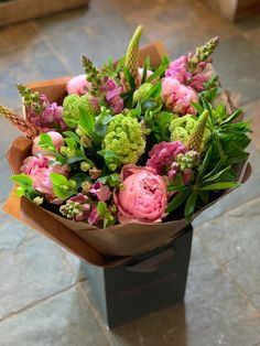 a bouquet of flowers sitting on top of a table next to a black box filled with green and pink flowers