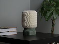 a white vase sitting on top of a wooden table next to a book and a potted plant