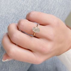 a woman's hand wearing a gold ring with an oval shaped diamond on it