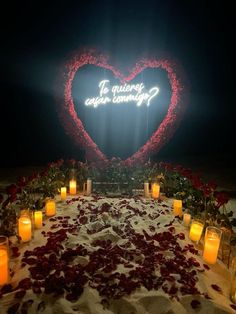 a heart - shaped sign with candles and roses on the ground in front of it