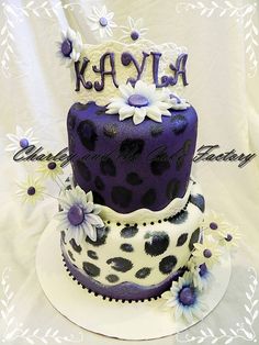 a three tiered cake with purple and white frosting, decorated with daisies