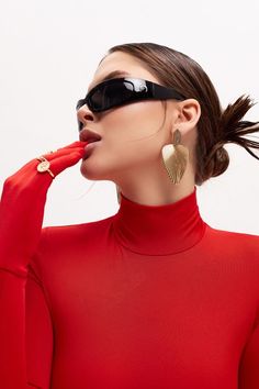 a woman in a red top and black sunglasses is holding her nose to her mouth