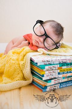 a baby sleeping on top of a stack of books with glasses on it's head