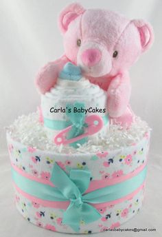 a pink teddy bear sitting on top of a diaper cake with a blue bow