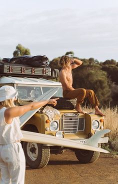 two people standing in front of a vehicle with luggage on top and one person sitting on the back