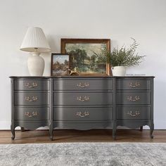 an antique dresser with two vases and a painting on the wall