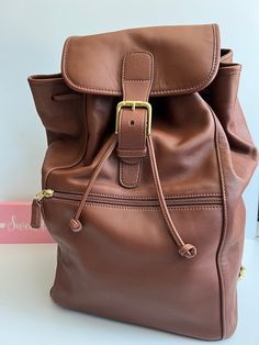 "Coach Travel Backpack  British tan Soft and Supple Leather with Brass Hardware Roomy lined interior with zippered pocket Closed by a drawstring and secured by a flap and buckle Outer front zip pocket Top handle Adjustable straps Hangtag and chain Made in China #B1293-00529 Measures: 10\"L base, 16\"H, 7.5\"W Cleaned, conditioned and ready to wear! B1" Everyday Backpack With Buckle Closure, Classic Brown Flap Backpack, Brown Travel Bags With Buckle Closure, Leather Travel Backpack With Buckle Closure, Leather Backpack With Buckle Closure, Travel Backpack With Buckle Closure, Leather Backpack With Buckle Closure For Everyday Use, Classic Travel Bags With Buckle Closure, Coach Backpack