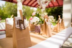 brown paper bags are lined up on a table with white flowers in the vases