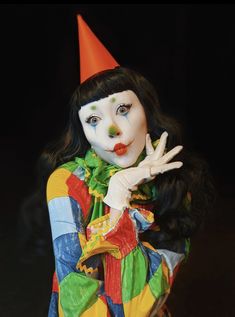 a woman dressed in clown makeup and holding her hand up to the side while making a peace sign