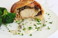 a white plate topped with meat and broccoli covered in gravy next to a glass of wine