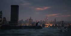 two people standing on top of a roof at night with city lights in the background