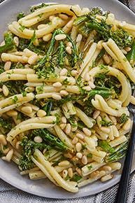 pasta with broccoli and pine nuts in a white bowl next to a fork