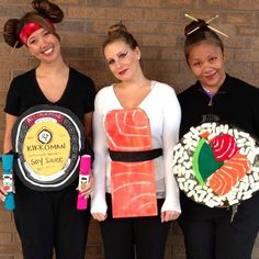 three women in costumes holding sushi plates and smiling at the camera while standing next to a brick wall